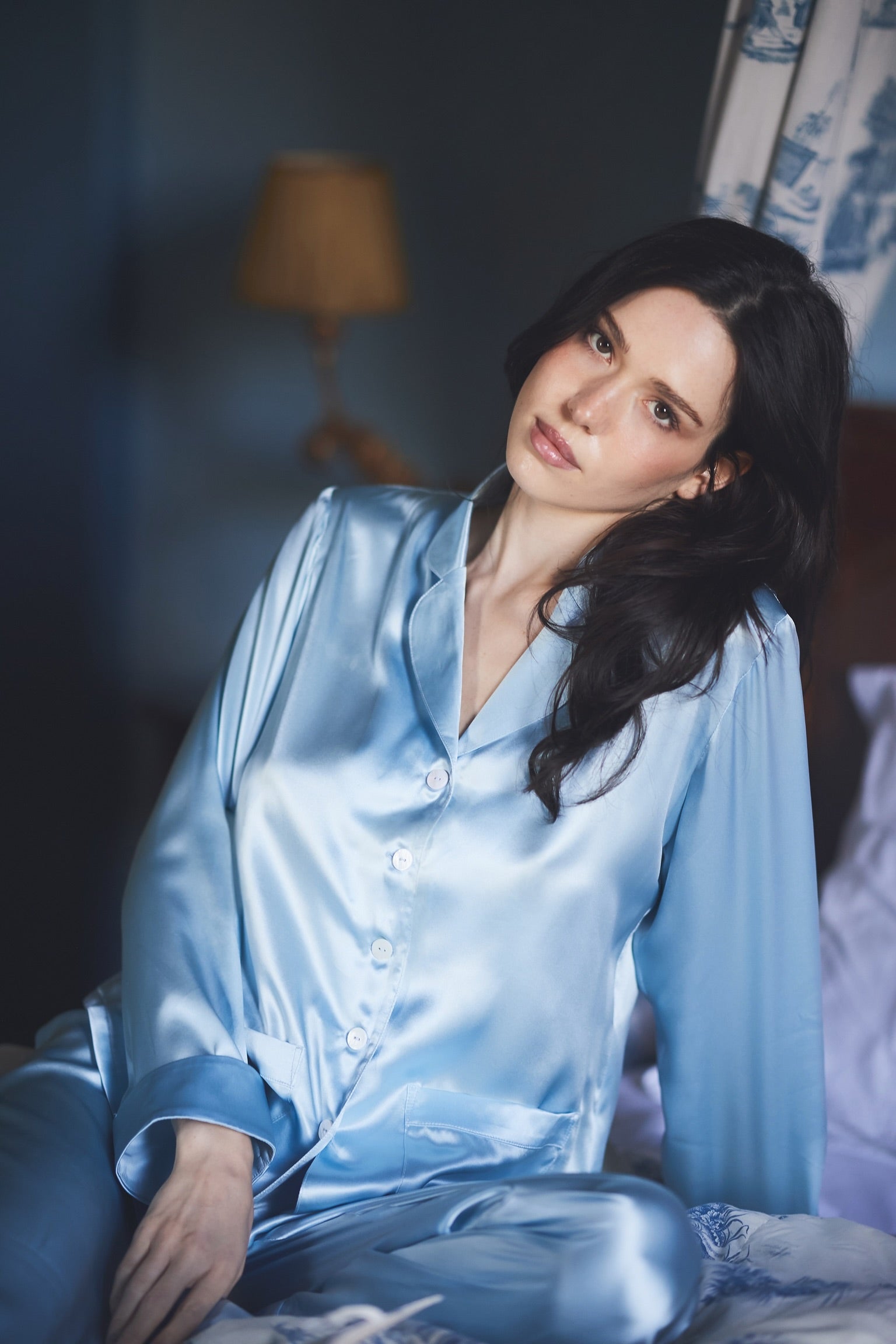 Woman in Cloud 9 blue silk pyjamas seated on a bed